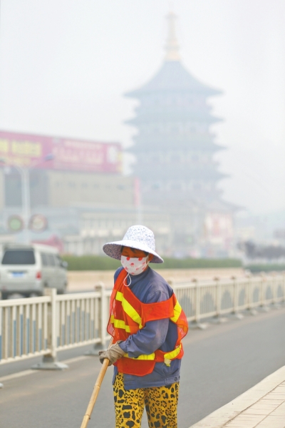 近日，在古都洛陽(yáng)，環(huán)衛(wèi)工人身后的“天堂”被霧霾籠罩著。
