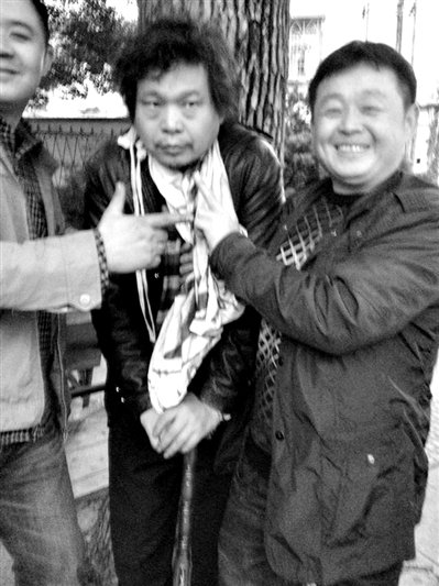 兩名接訪人員與患有癌癥的訪民段新德合影時(shí)，面帶笑容擺出勝利的手勢(shì)。