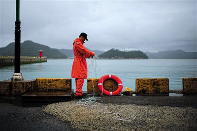7月6日，韓國(guó)珍島，一名海岸警察在港口系救生圈。4月，客輪在珍島近海發(fā)生沉船事故后，仍有11人下落不明。