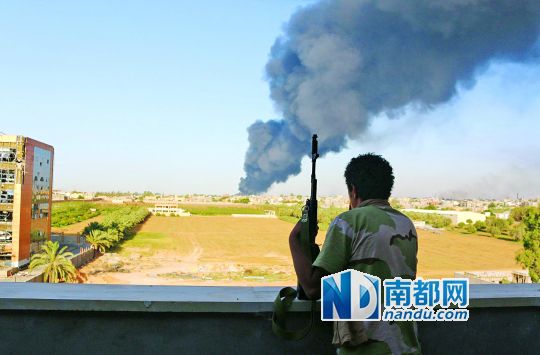 2日，利比亞首都的黎波里，一民兵武裝成員眺望被火箭彈擊中的儲油罐冒出濃煙。