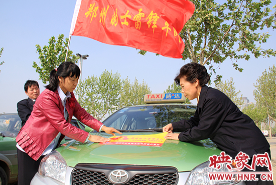 　　授旗結(jié)束后，首都的士雷鋒車隊(duì)王鳳進(jìn)隊(duì)長（右）與鄭州的的哥的姐在車身上貼上標(biāo)識。