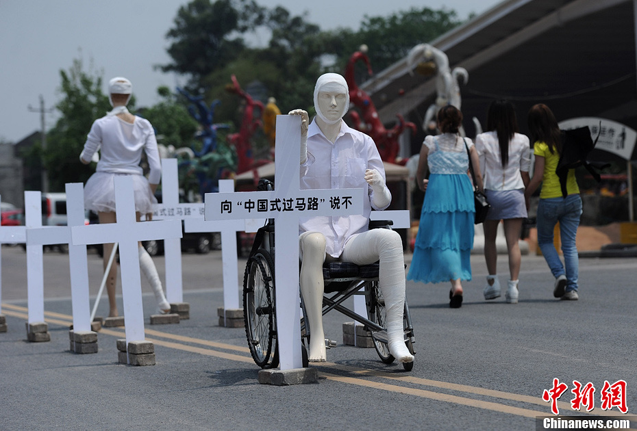 4月16日，重慶市洋人街上擺放著兩個(gè)受了傷的塑料人像“模特”，旁邊十字架上寫(xiě)著向“中國(guó)式過(guò)馬路”說(shuō)不