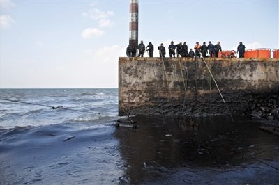 昨日，山東青島，清污人員正在海邊清理油污。
