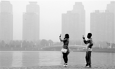 29日中午，鄭東新區(qū)如意湖畔，兩個年輕人拍攝霧霾中的景色。 鄭州晚報記者 馬健 圖