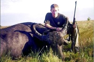 哈里王子手持獵槍，蹲在一頭遭到獵殺的水牛旁邊