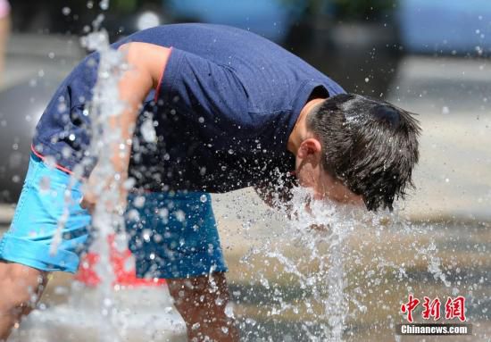 5月29日，一名小孩將頭伸向北京街頭的噴泉以降溫祛暑。