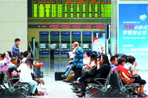 候車大廳溫度很高，一名乘客一手扇風(fēng)、一手擦汗