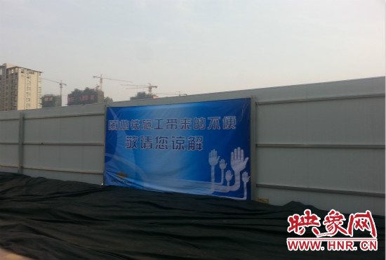 道路南側(cè)圍起了白色的圍擋，墻上標(biāo)示著“因地鐵施工帶來的不便敬請(qǐng)您諒解”的提示牌。
