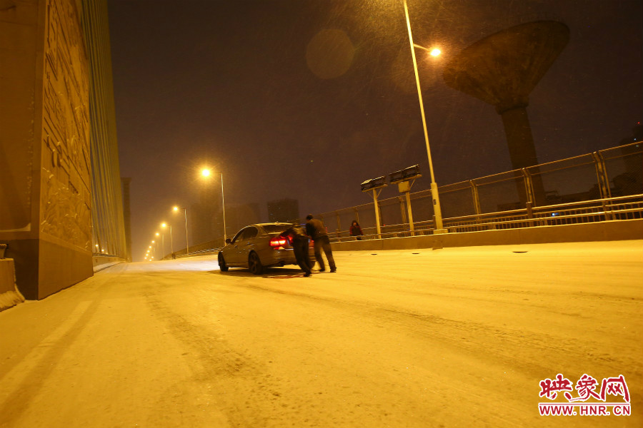 雪天路滑，汽車上橋打滑，兩名“推車人”幫助一輛私家車上坡。