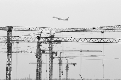 空中是起飛的飛機(jī)，下面是T2航站樓工地上林立的塔吊