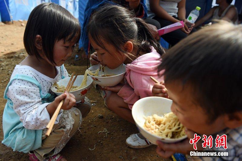 2014年8月6日，云南魯?shù)辇堫^山災(zāi)區(qū)，兒童在帳篷外吃飯。