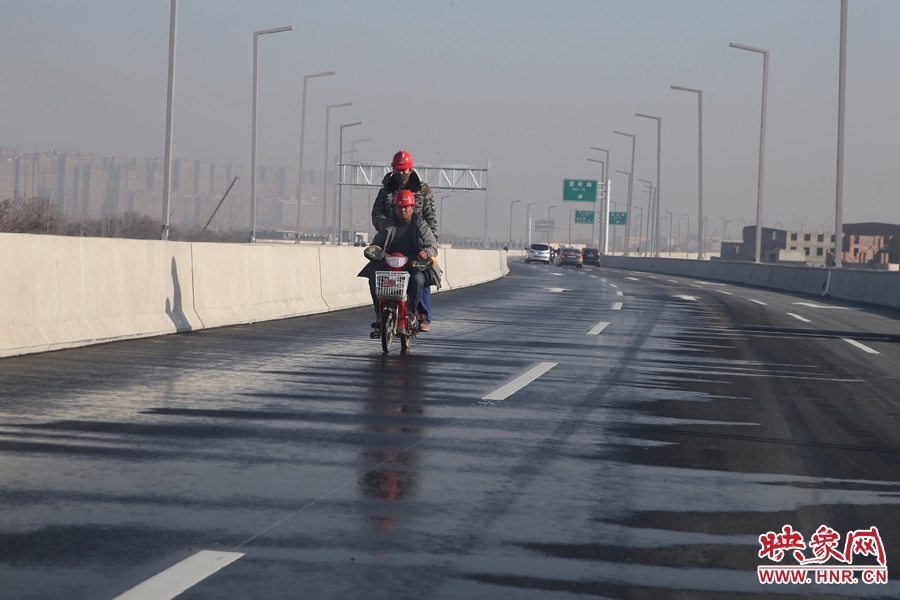 兩名工人騎車經(jīng)過灑水養(yǎng)護(hù)路面。