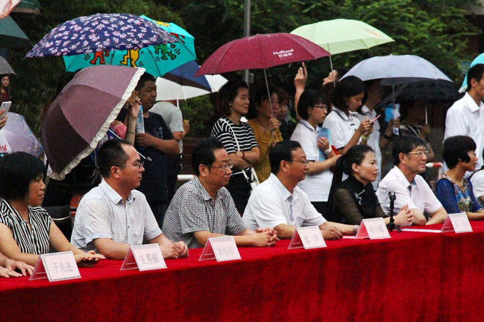 在主席臺上觀看的校領導也堅持不打傘陪學生一起淋雨，身旁站滿了打傘觀看的家長。